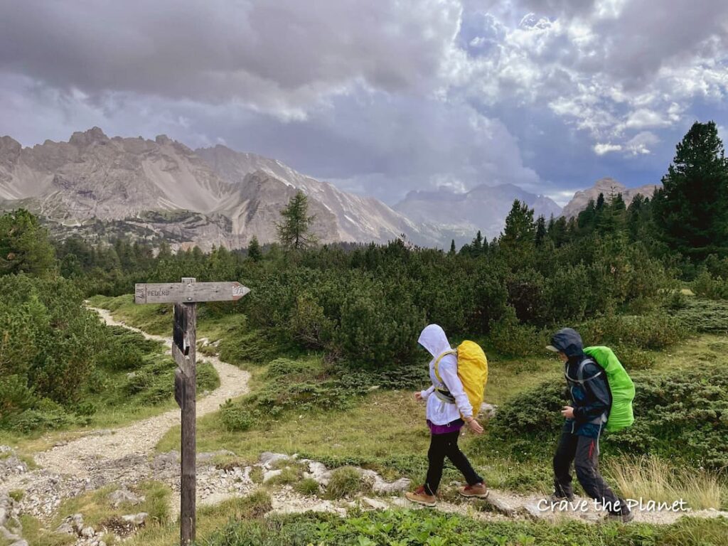 two girls hiking in the dolomites in the rain on a stony trail 