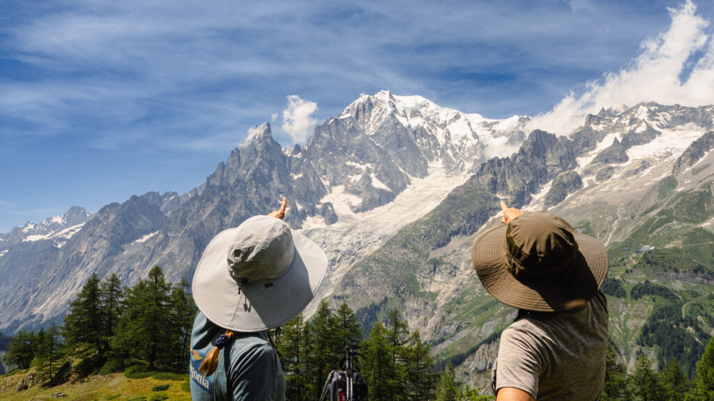 two women pointing to mt blanc on a hike. both wearing cool hats